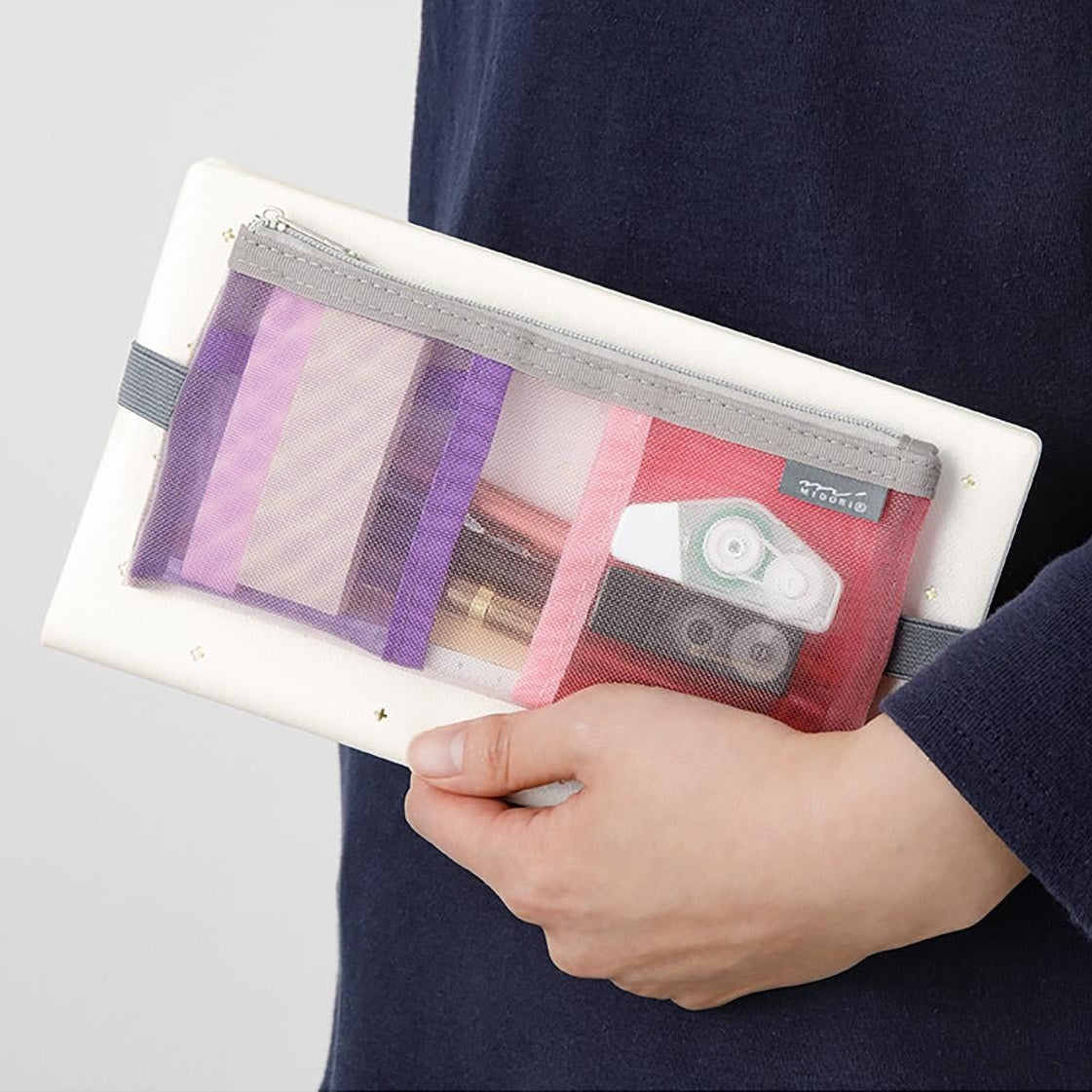 Person holding a transparent pouch with stationery items inside, against a neutral background.
